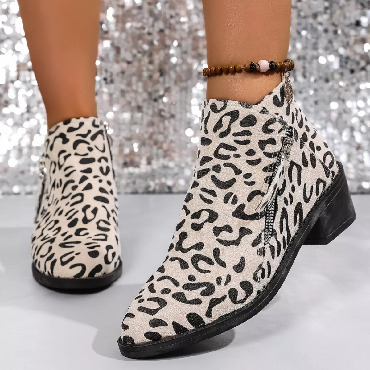 Woman wearing beige leopard-print ankle boots with block heels and side zipper details.