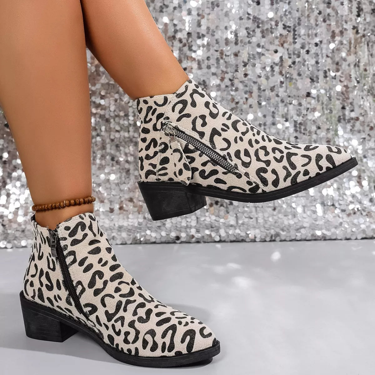 Woman wearing beige leopard-print ankle boots with block heels and side zipper details.