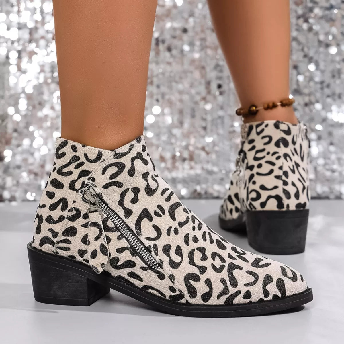 Woman wearing beige leopard-print ankle boots with block heels and side zipper details.