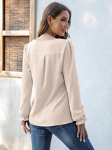 Woman wearing a beige notched neck long sleeve blouse with flounce cuffs styled with light-wash jeans.