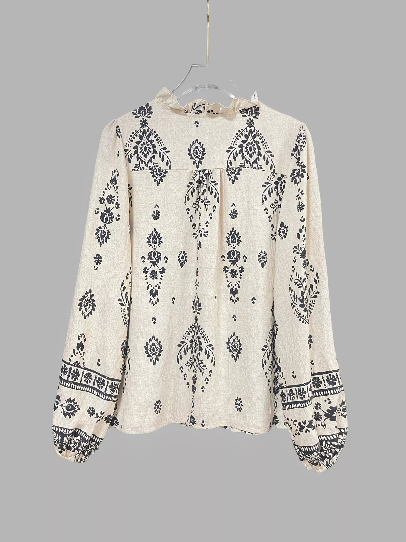 Woman wearing a beige and black vintage print long-sleeve blouse with dark denim jeans, a brown belt, and statement jewelry.