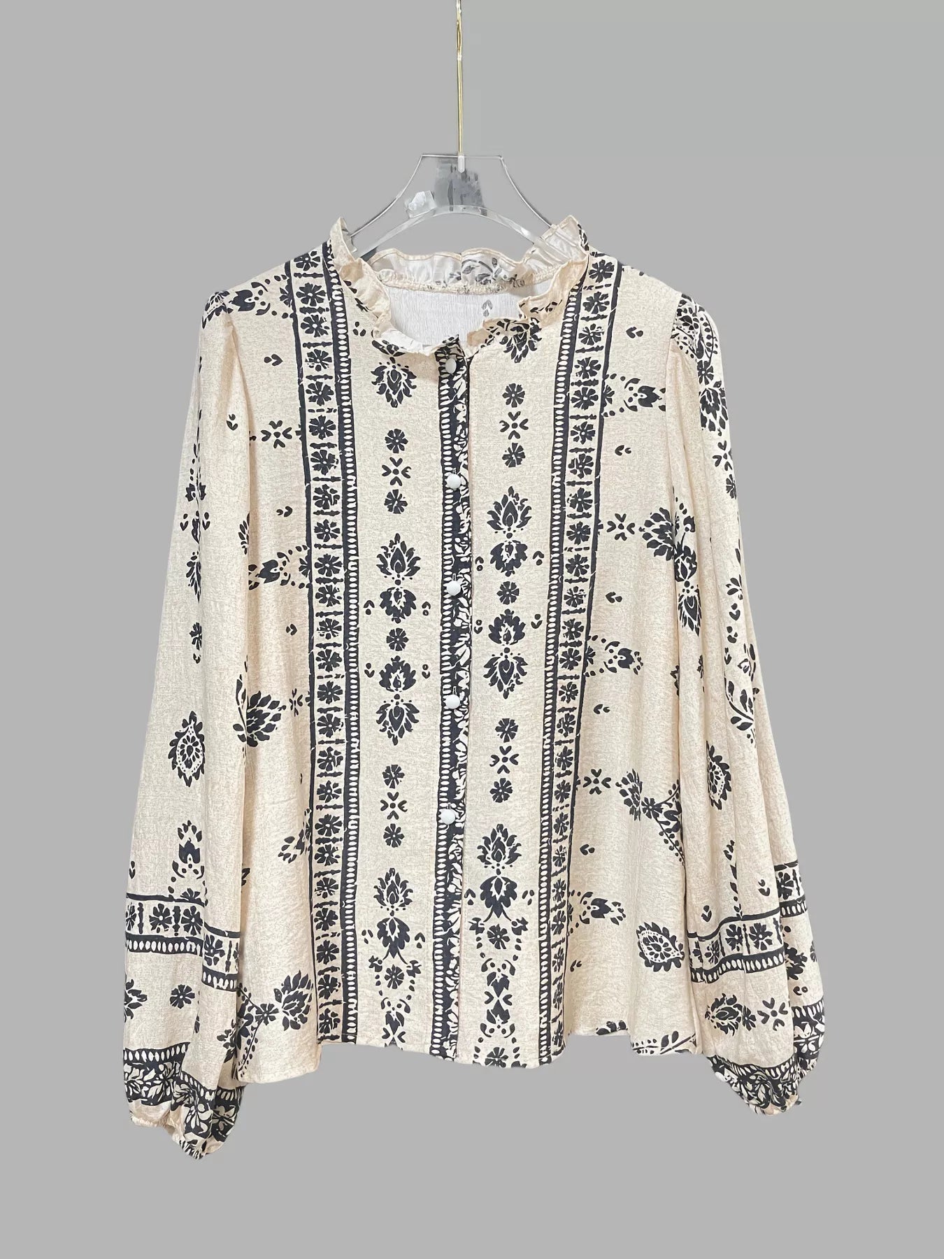 Woman wearing a beige and black vintage print long-sleeve blouse with dark denim jeans, a brown belt, and statement jewelry.