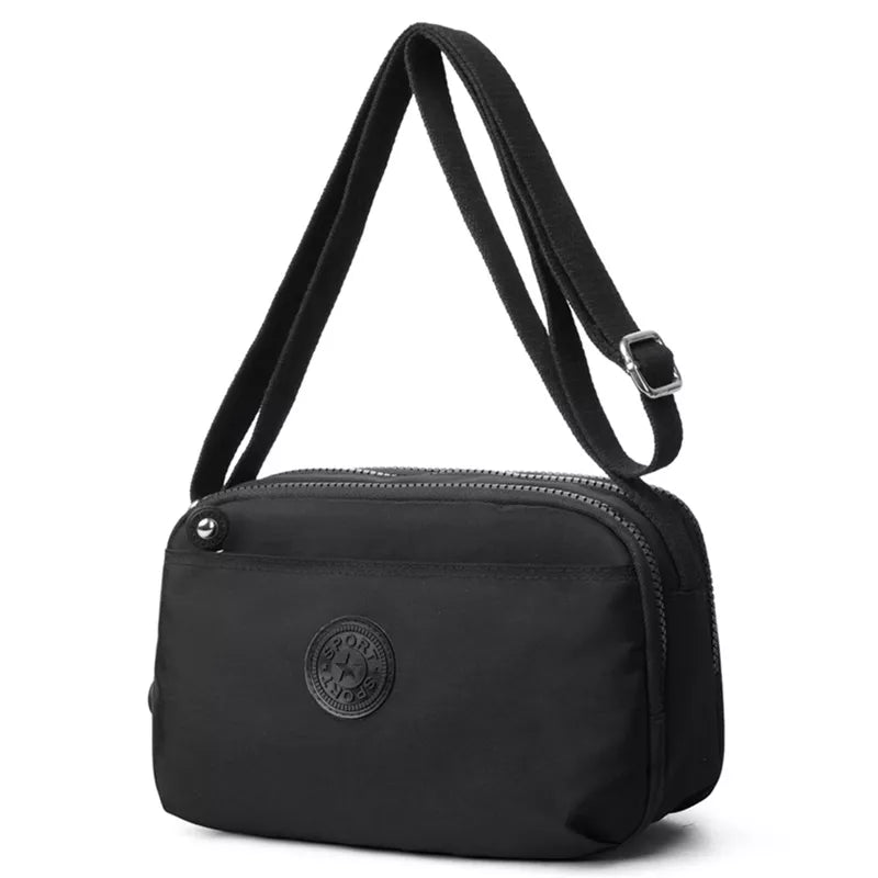 Small black nylon crossbody bag with an adjustable matching strap, silver-tone buckle, zippered top closure, and front pocket detail.