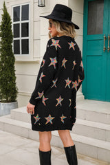 Woman wearing a black open-front cardigan with colorful star print, front pockets, denim shorts and black Western boots.