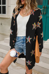 Woman wearing a black open-front cardigan with colorful star print, front pockets, denim shorts and black Western boots.