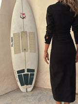 Woman wearing a black button-front midi dress with gold-tone buttons, collared neckline, patch pockets, fitted seam details and front slit.