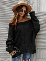 Woman wearing a black cable knit openwork off-shoulder sweater with distressed jeans and a wide-brim hat.