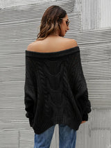 Woman wearing a black cable knit openwork off-shoulder sweater with distressed jeans and a wide-brim hat.