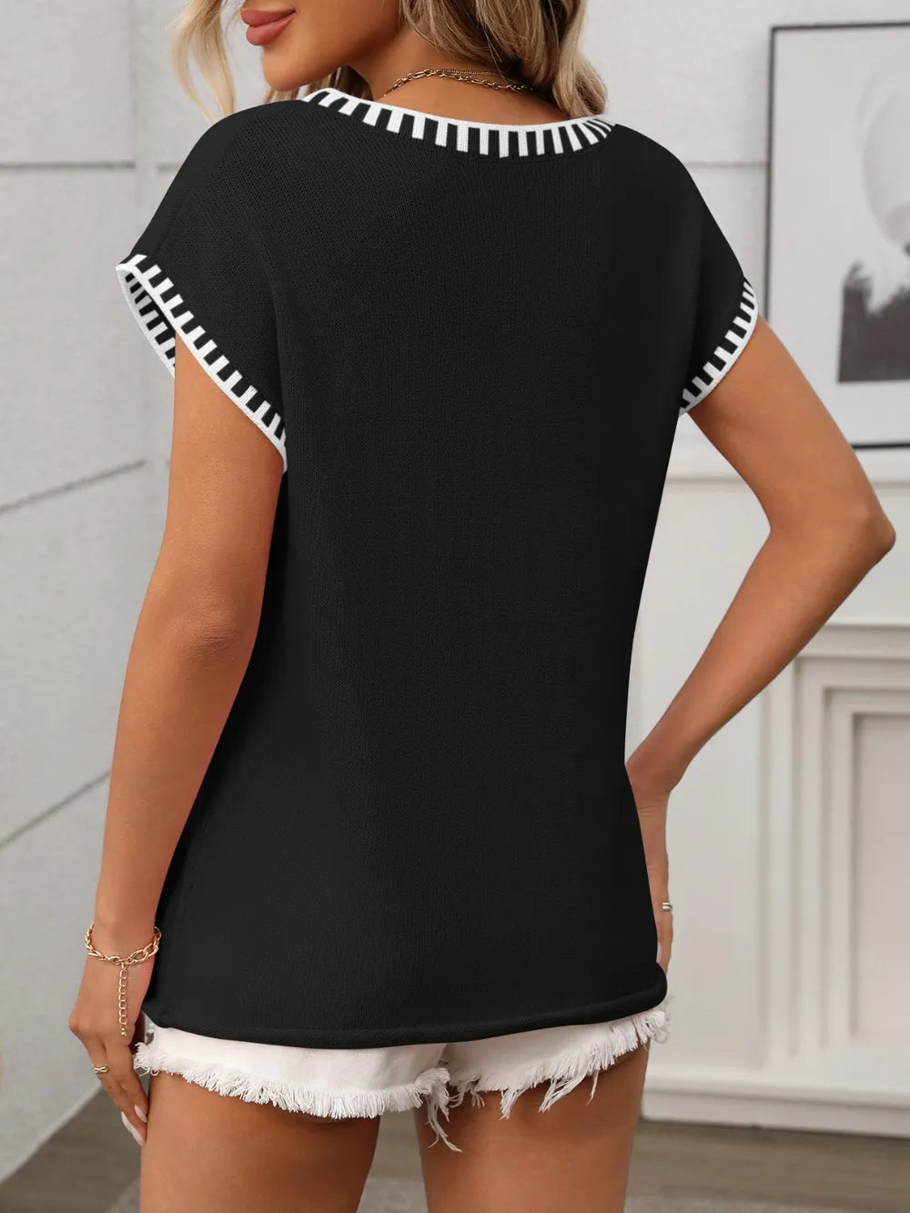 Woman wearing a black short sleeve knit top with white contrast trim along the V-neckline and sleeves.