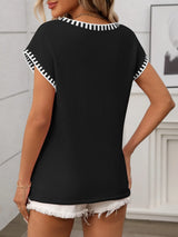 Woman wearing a black short sleeve knit top with white contrast trim along the V-neckline and sleeves.