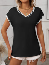 Woman wearing a black short sleeve knit top with white contrast trim along the V-neckline and sleeves.