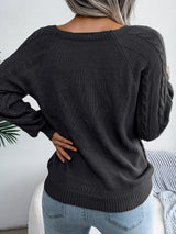 Woman wearing a black cable-knit sweater with decorative buttons, paired with light-wash jeans, layered gold necklaces, and a white handbag. Perfect for cozy fall and winter outfits.
