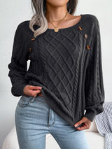 Woman wearing a black cable-knit sweater with decorative buttons, paired with light-wash jeans, layered gold necklaces, and a white handbag. Perfect for cozy fall and winter outfits.