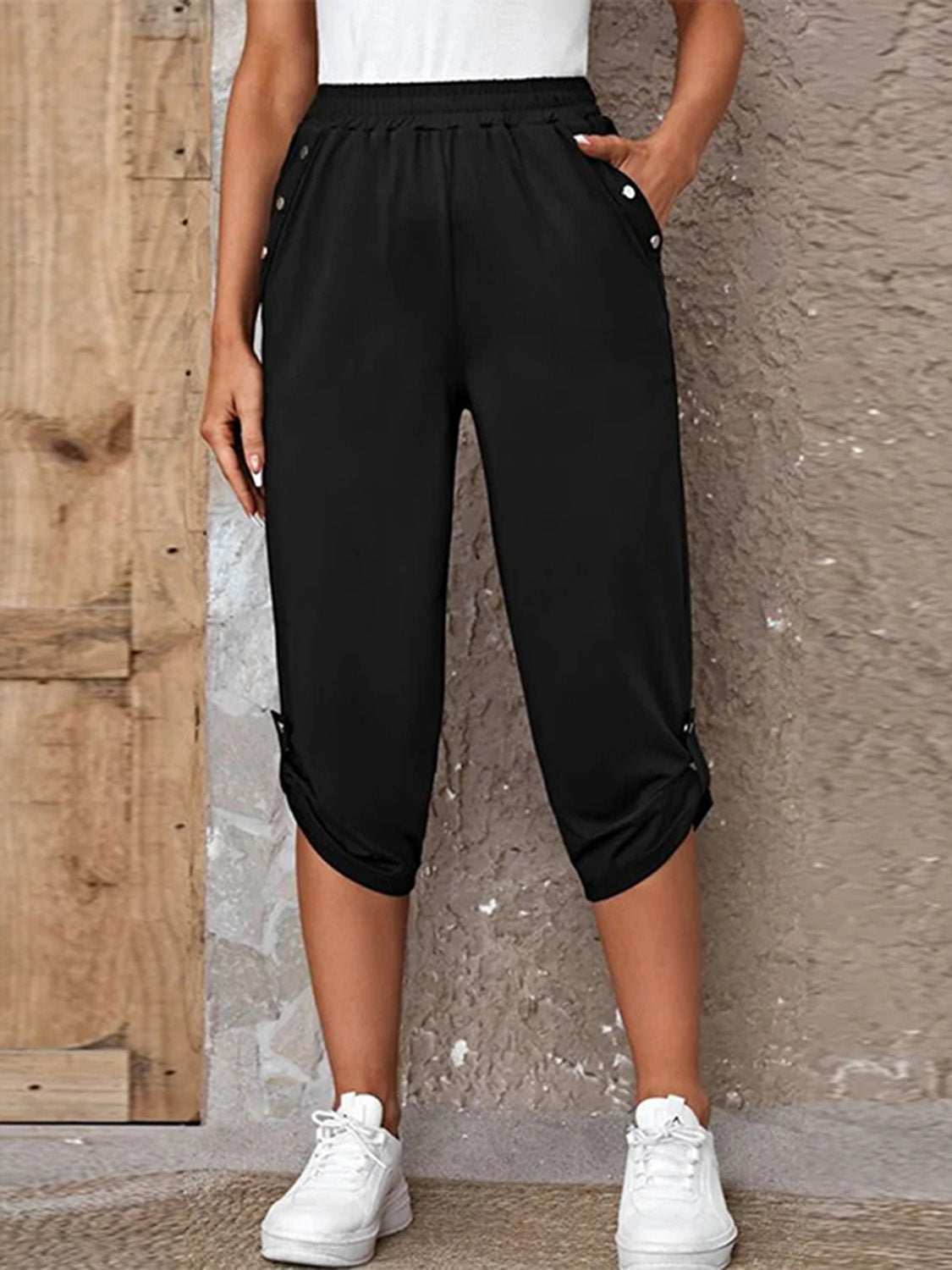 Model wearing black roll-tab capri pants with side pockets and white sneakers for a casual outdoor look.