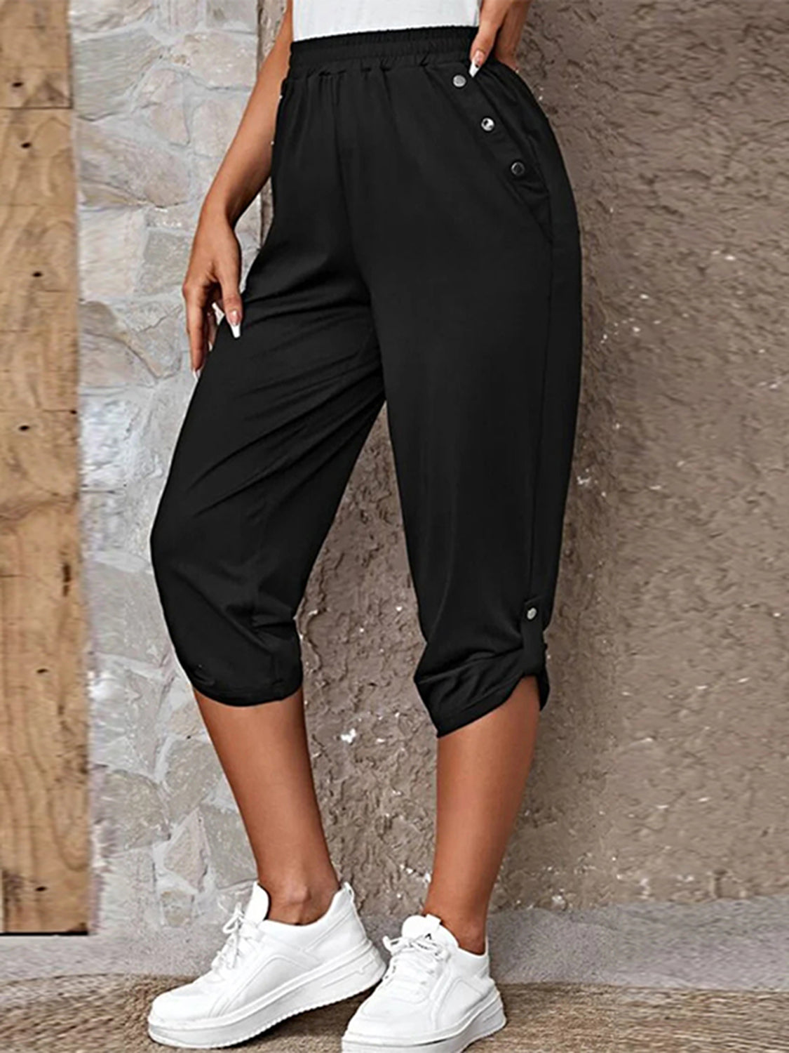 Model wearing black roll-tab capri pants with side pockets and white sneakers for a casual outdoor look.