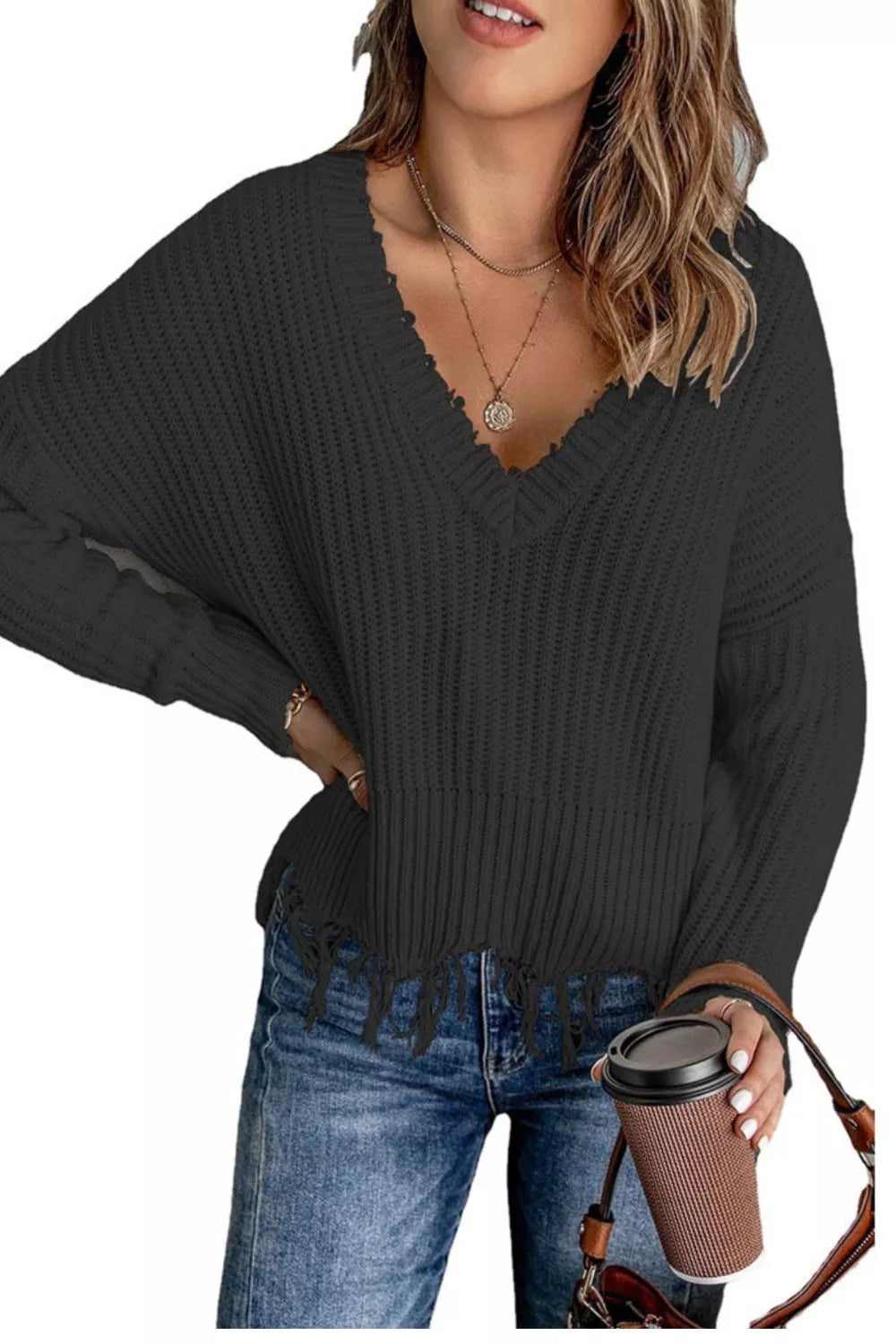 Woman wearing a black ribbed V-neck sweater with distressed raw hem and blue jeans.