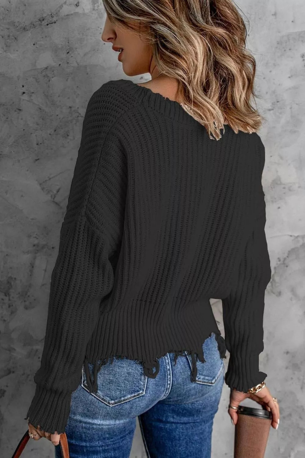 Woman wearing a black ribbed V-neck sweater with distressed raw hem and blue jeans.