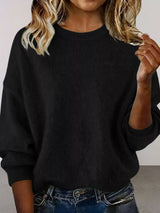 Woman wearing a black round neck dropped shoulder sweater with dark-wash jeans.