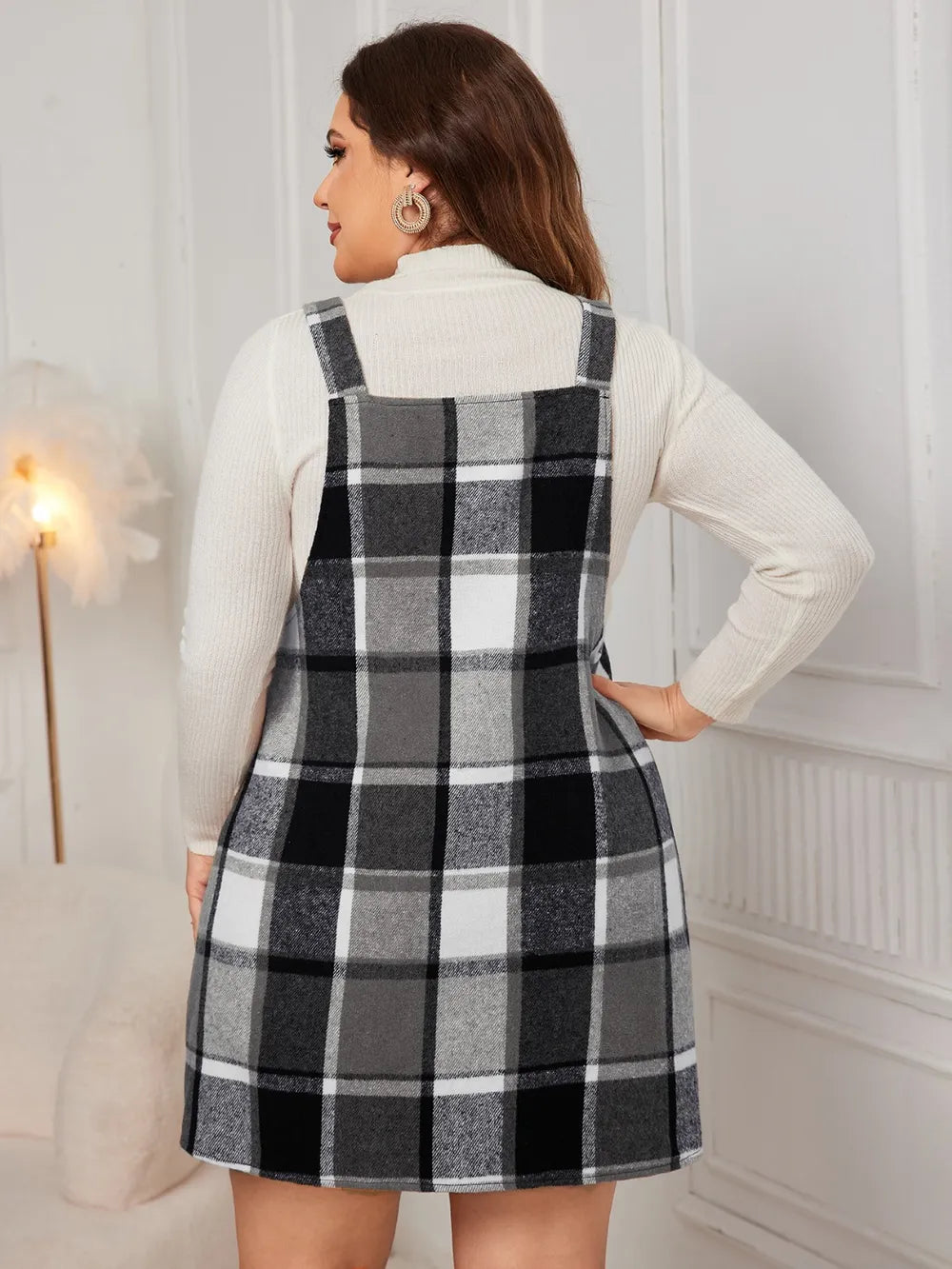 Woman wearing the Honey Plus Size Plaid Wide Strap Overall Dress layered over a cream mock neck sweater with a black felt hat, stylish plus size plaid fall dress from Chic Mystik Boutique.