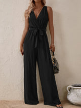 Woman wearing the Honey Tied Surplice Sleeveless Wide Leg Jumpsuit in black with a tie waist and wide-leg silhouette, elegant women's one-piece outfit from Chic Mystik Boutique.