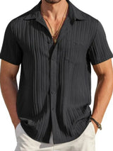 Man wearing a black textured short sleeve button-up shirt with white pants for a polished casual summer look.