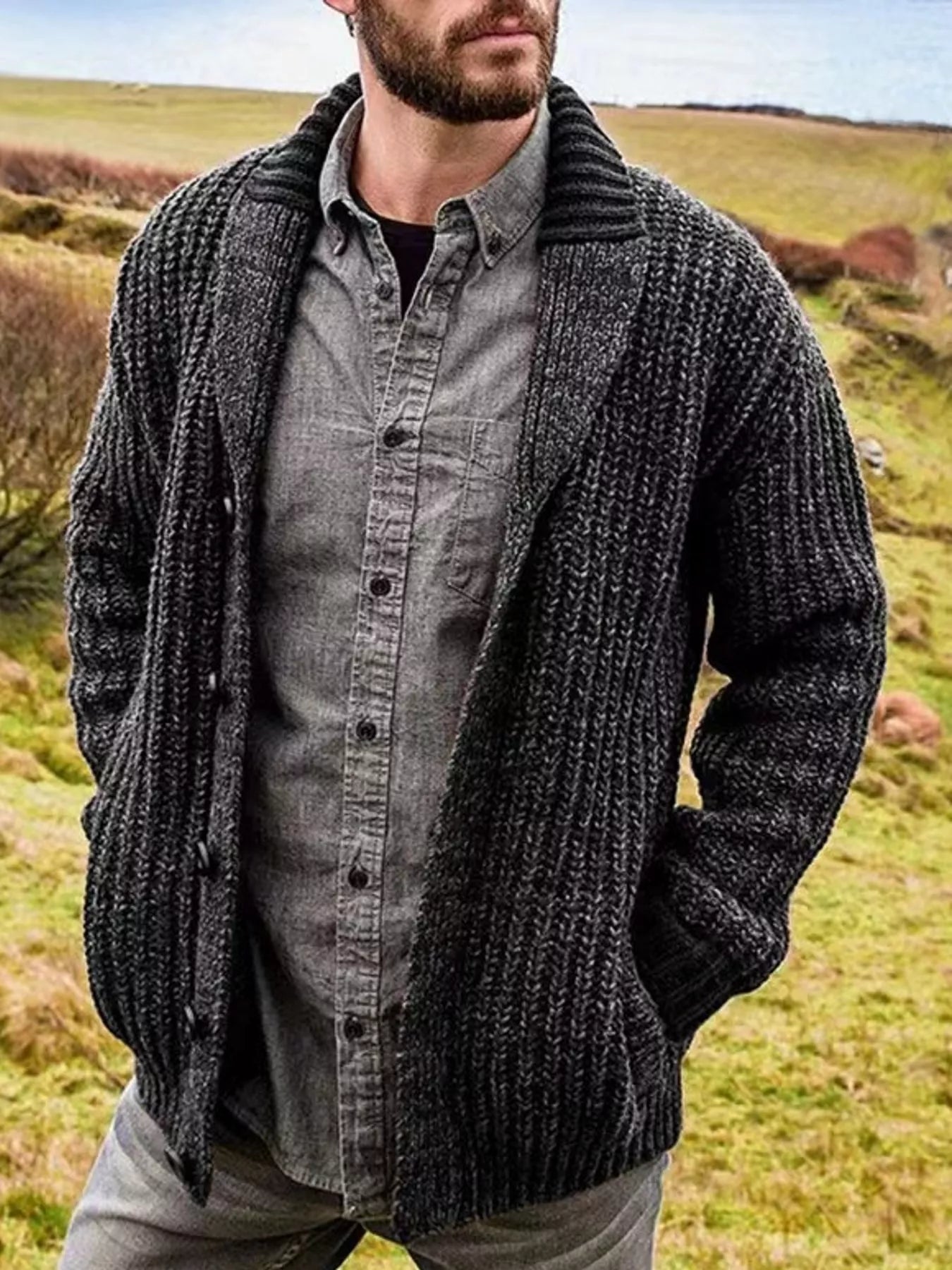 Men's black chunky knit shawl collar cardigan with button-front closure, ribbed texture, and front pockets, layered over a gray button-down shirt.
