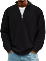 Man wearing a black ribbed corduroy quarter zip pullover sweatshirt layered over a white shirt.