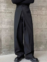 Men's black wide leg pleated pants with a button-front waistband and relaxed, full-length silhouette, styled with a black top and chunky black shoes.