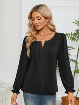 Woman wearing a black notched neck long sleeve blouse with flounce cuffs styled with light-wash jeans and a black handbag.