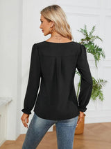 Woman wearing a black notched neck long sleeve blouse with flounce cuffs styled with light-wash jeans and a black handbag.