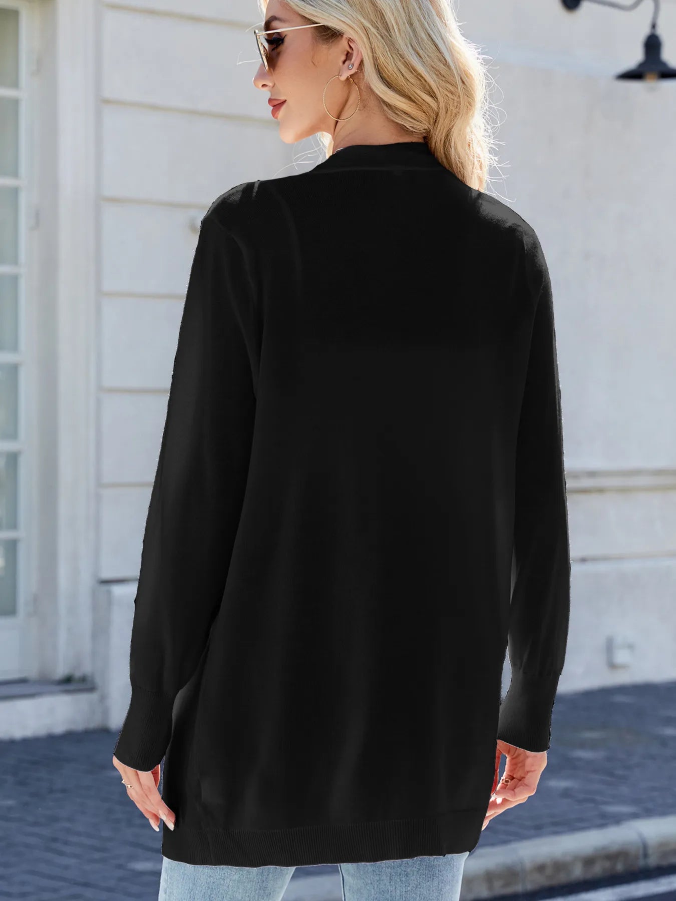 Woman wearing a black open front cardigan with blue jeans, layered over a white tank top for a casual everyday outfit.
