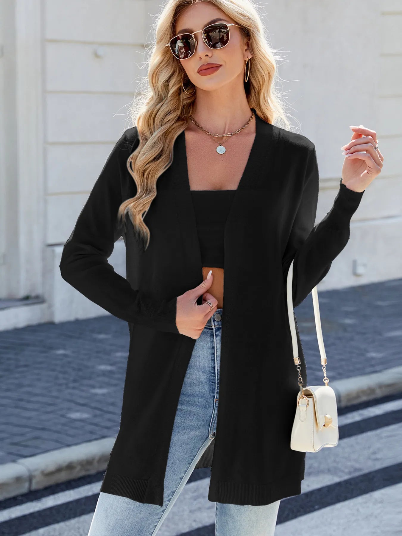 Woman wearing a black open front cardigan with blue jeans, layered over a white tank top for a casual everyday outfit.