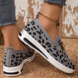 Leopard print slip-on sneakers with gold accents worn by a person on a textured surface.