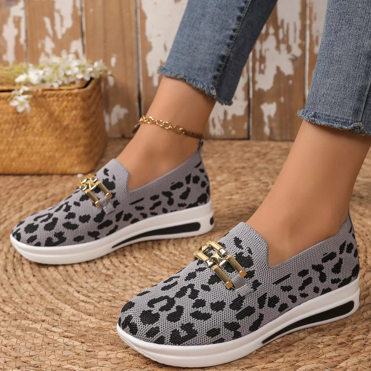Gray leopard print shoes with gold accents worn by a person on a woven surface.