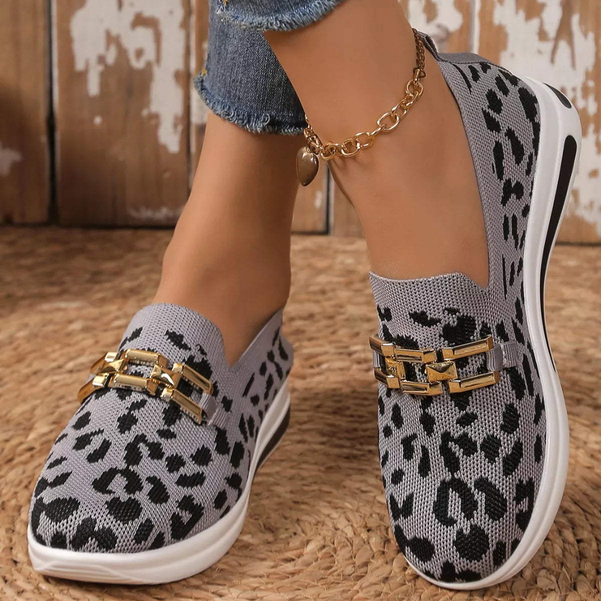 Leopard print slip-on shoes with gold accents worn by a person on a textured surface.