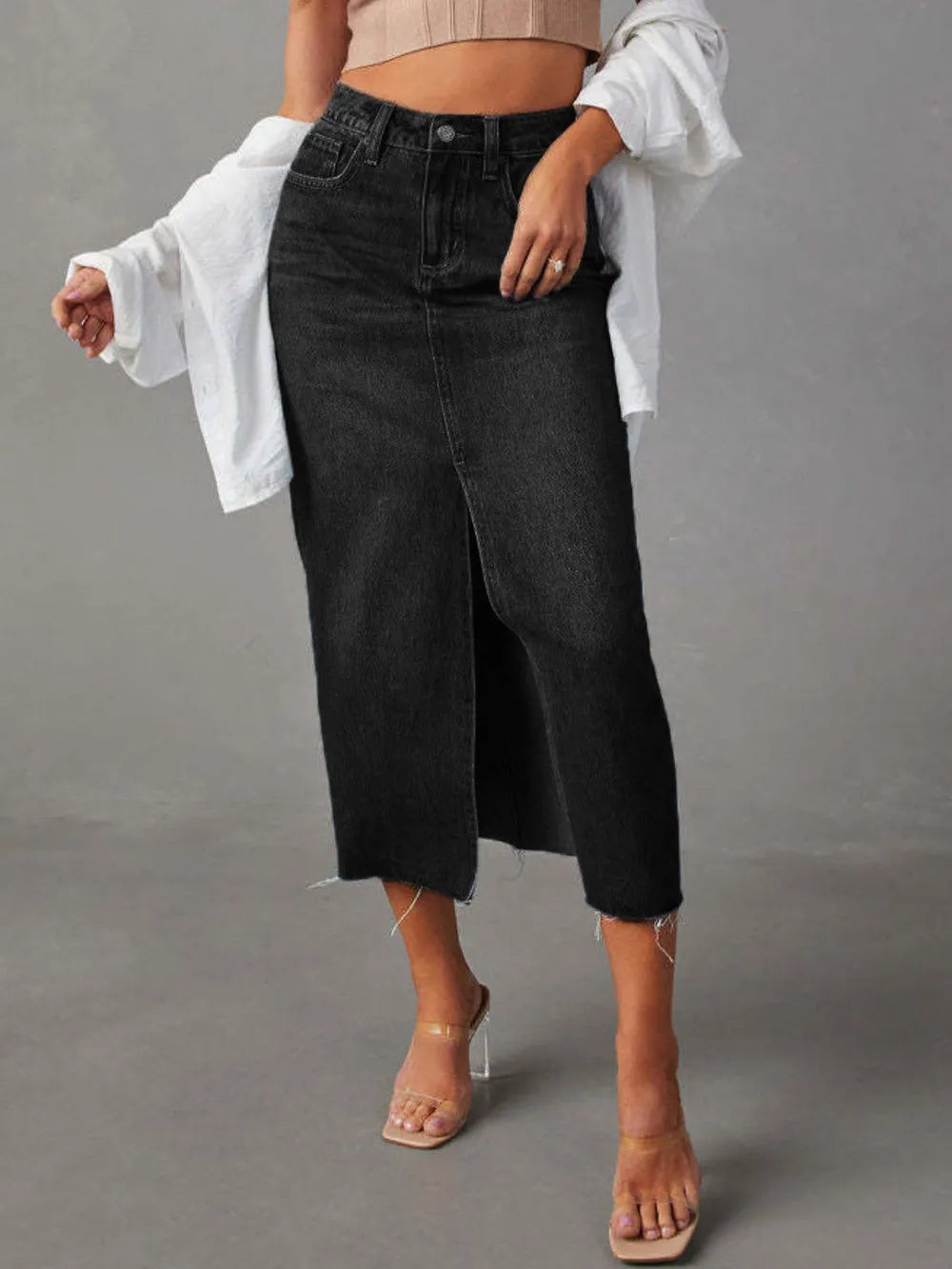 Woman wearing a black wash denim midi skirt with front slit, pockets and raw hem.