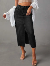 Woman wearing a black wash denim midi skirt with front slit, pockets and raw hem.
