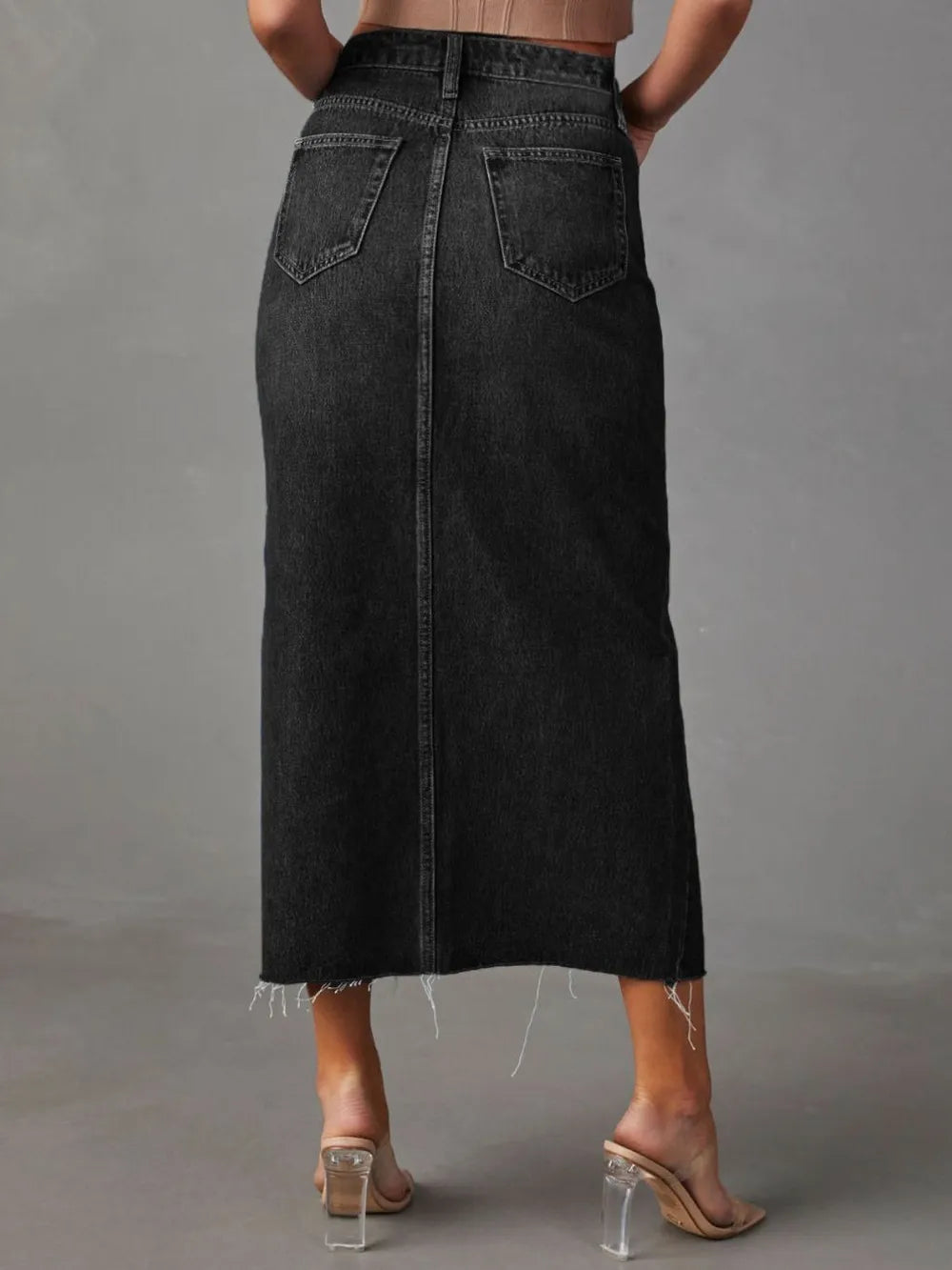 Woman wearing a black wash denim midi skirt with front slit, pockets and raw hem.