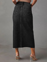 Woman wearing a black wash denim midi skirt with front slit, pockets and raw hem.