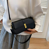 Black rectangular crossbody handbag with a gold turn-lock buckle and adjustable shoulder strap displayed on a modern tabletop.
