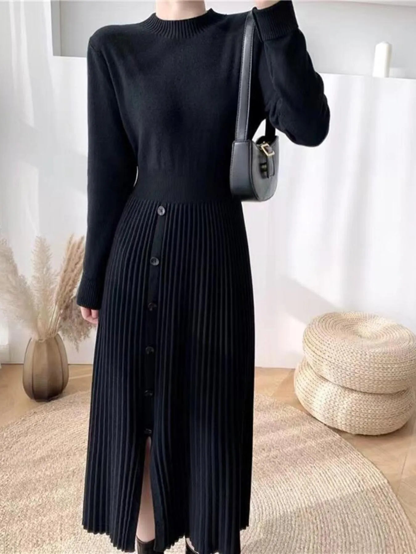 Woman wearing a black mock neck long sleeve knit midi dress with pleated skirt, front buttons and slit.