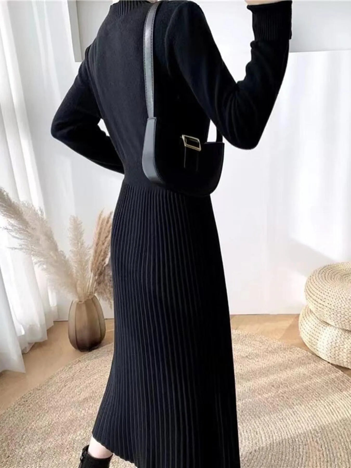 Woman wearing a black mock neck long sleeve knit midi dress with pleated skirt, front buttons and slit.
