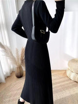 Woman wearing a black mock neck long sleeve knit midi dress with pleated skirt, front buttons and slit.