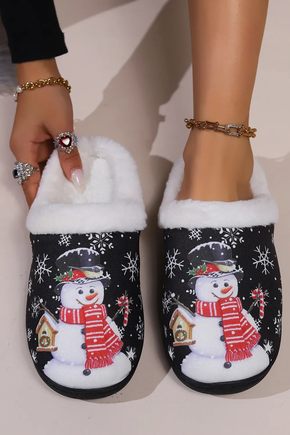 Black snowman round toe slippers with white faux fur trim, festive snowflake print, red scarf design, and black flat soles.