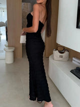 Woman wearing a black sweetheart neck tube maxi dress with ruched detailing and a subtle cutout, styled with an ivory clutch for an elegant evening look.