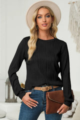 Woman wearing a black textured round neck long sleeve blouse with dark-wash jeans, brown clutch and cream hat.