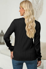 Woman wearing a black textured round neck long sleeve blouse with dark-wash jeans.