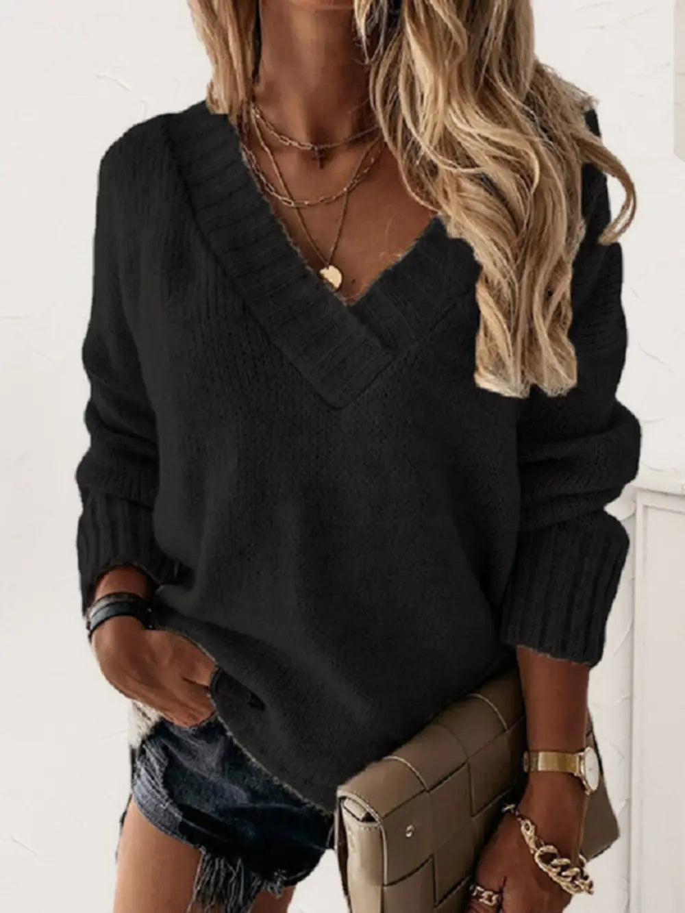 Woman wearing a black V-neck long sleeve knit top with ribbed neckline and cuffs, styled with black denim shorts.