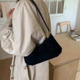 Black suede vintage-style shoulder bag with a minimalist silhouette paired with a neutral outfit.