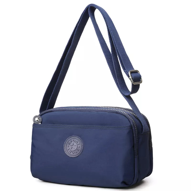 Small blue nylon crossbody bag with an adjustable matching strap, silver-tone buckle, zippered top closure, and front pocket detail.